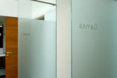 Een moderne kantooringang met deuren van matglas, een houten deur en een witte muur, wat zorgt voor een strakke en professionele sfeer.