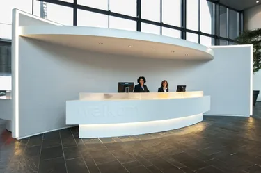 Een strakke en moderne receptie met een witte ronde balie waaraan twee vrouwen in zakelijke kleding aan het werk zijn.