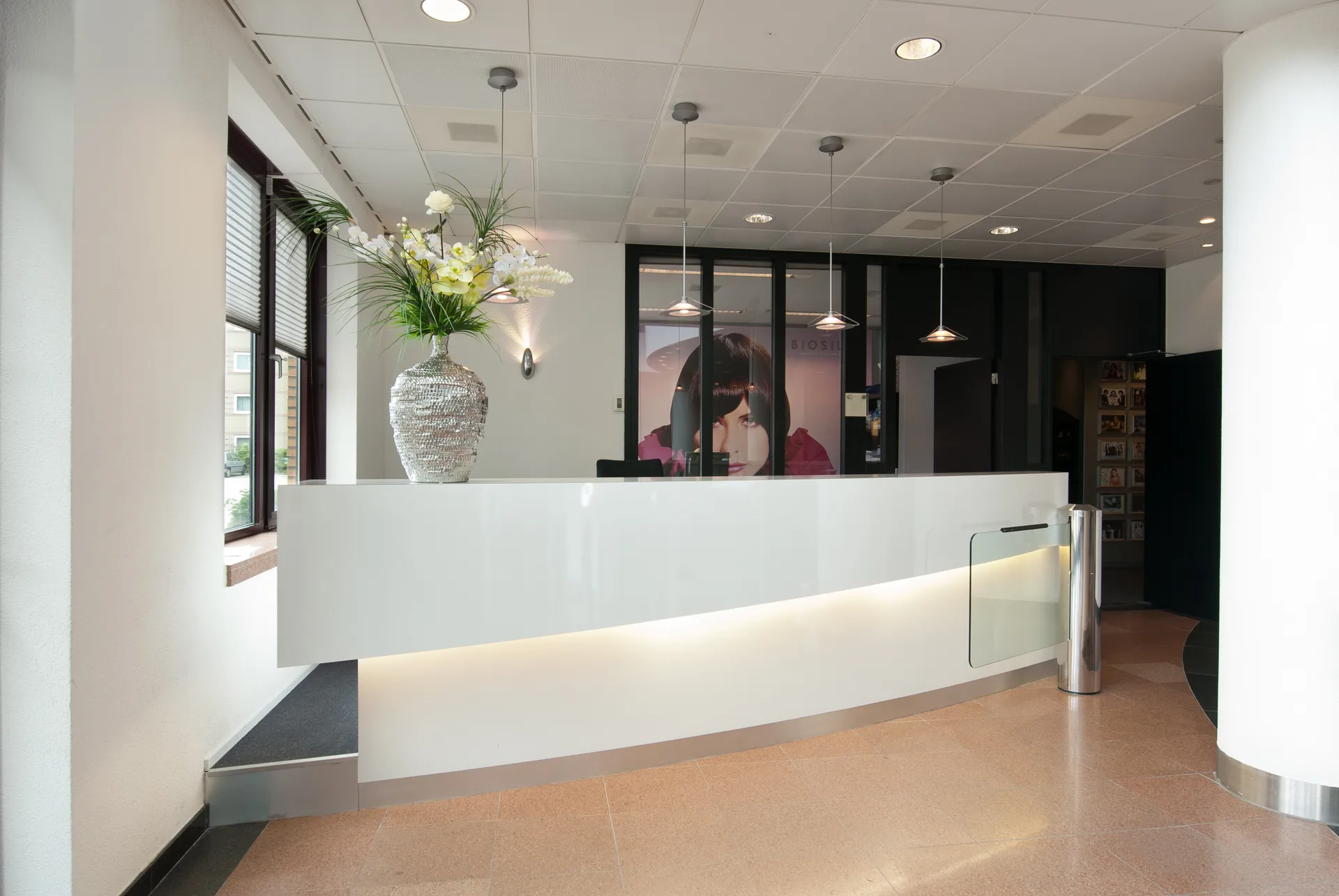 Een strakke en moderne kantoorreceptie met een witte ontvangstbalie, een groot raam en een prachtig bloemstuk.