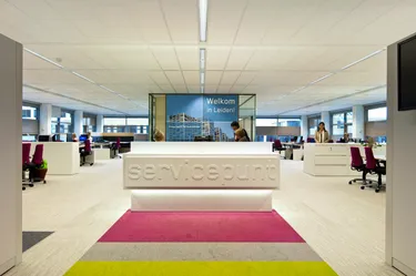 Een moderne kantoorruimte met een witte receptiebalie en een groot scherm met een welkomstbericht, wat een warme sfeer creëert voor medewerkers en bezoekers.