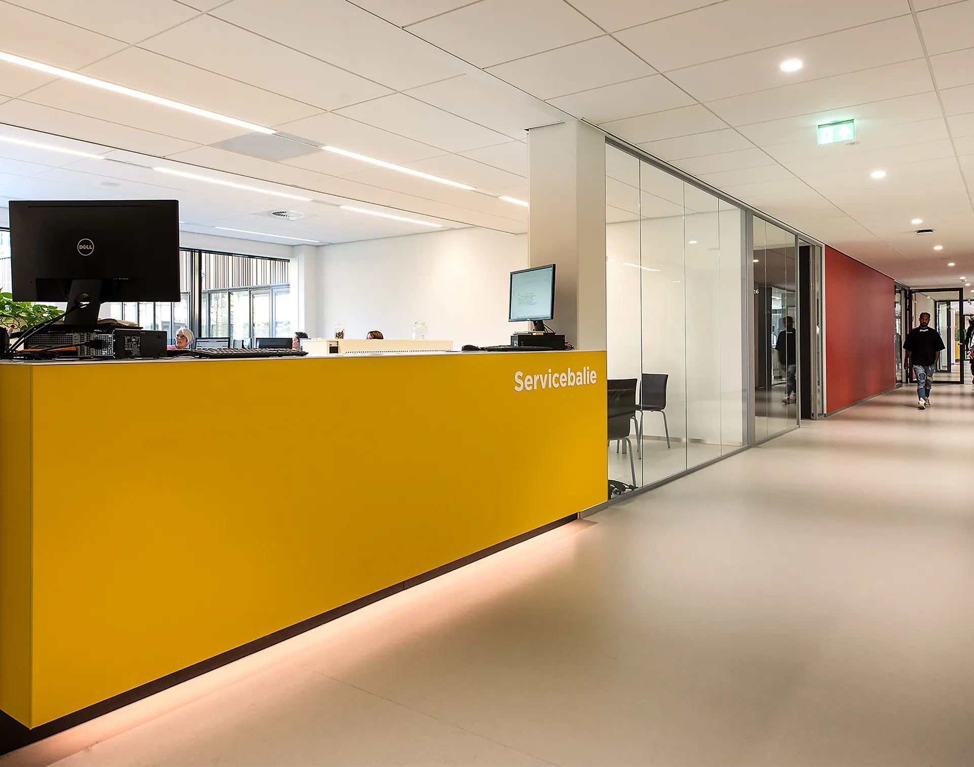 Servicebalie met gele voorkant en een glazen wand in een modern kantoor.