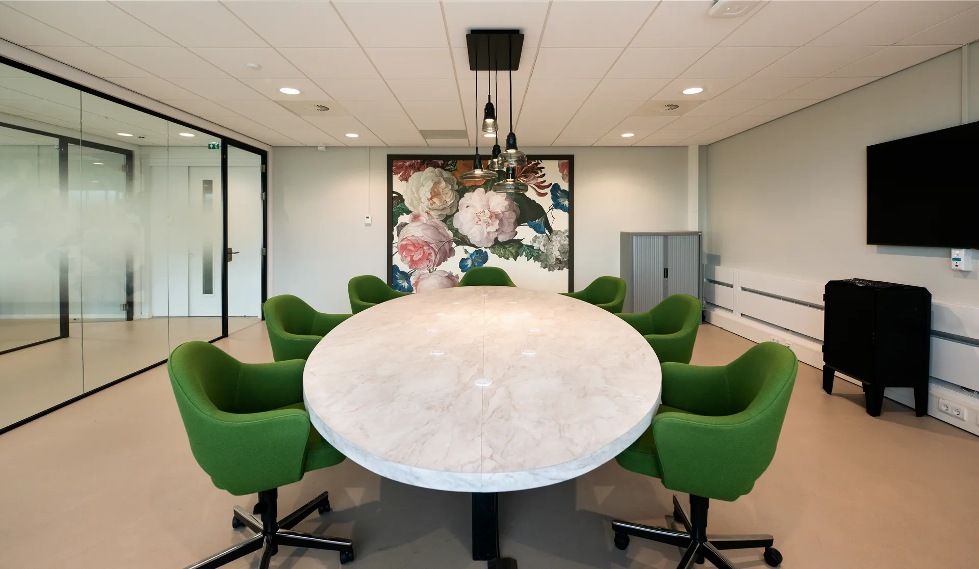 Een moderne vergaderruimte met een grote witte tafel, groene stoelen en een tv-scherm aan de muur.