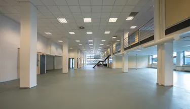 Een grote, open kantoorruimte met witte muren, grijze vloeren en een hoog plafond. De ruimte is leeg, zonder meubilair of apparatuur.