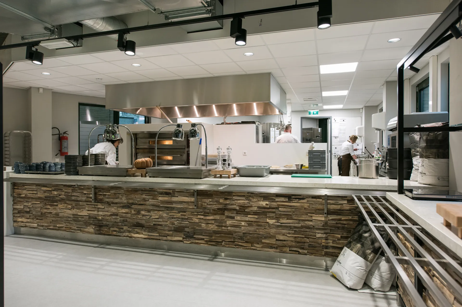 Een commerciële bedrijfskeuken met een groot kookeiland in het midden, met diverse apparatuur zoals een grote oven en een koelkast.