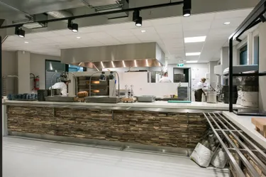 Een commerciële bedrijfskeuken met een groot kookeiland in het midden, met diverse apparatuur zoals een grote oven en een koelkast.