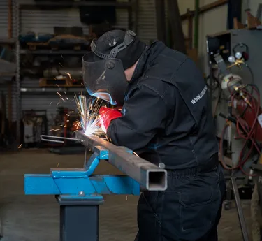 Een persoon in beschermende kleding last metaal in een industriële werkplaats, waarbij veel vonken vrijkomen.