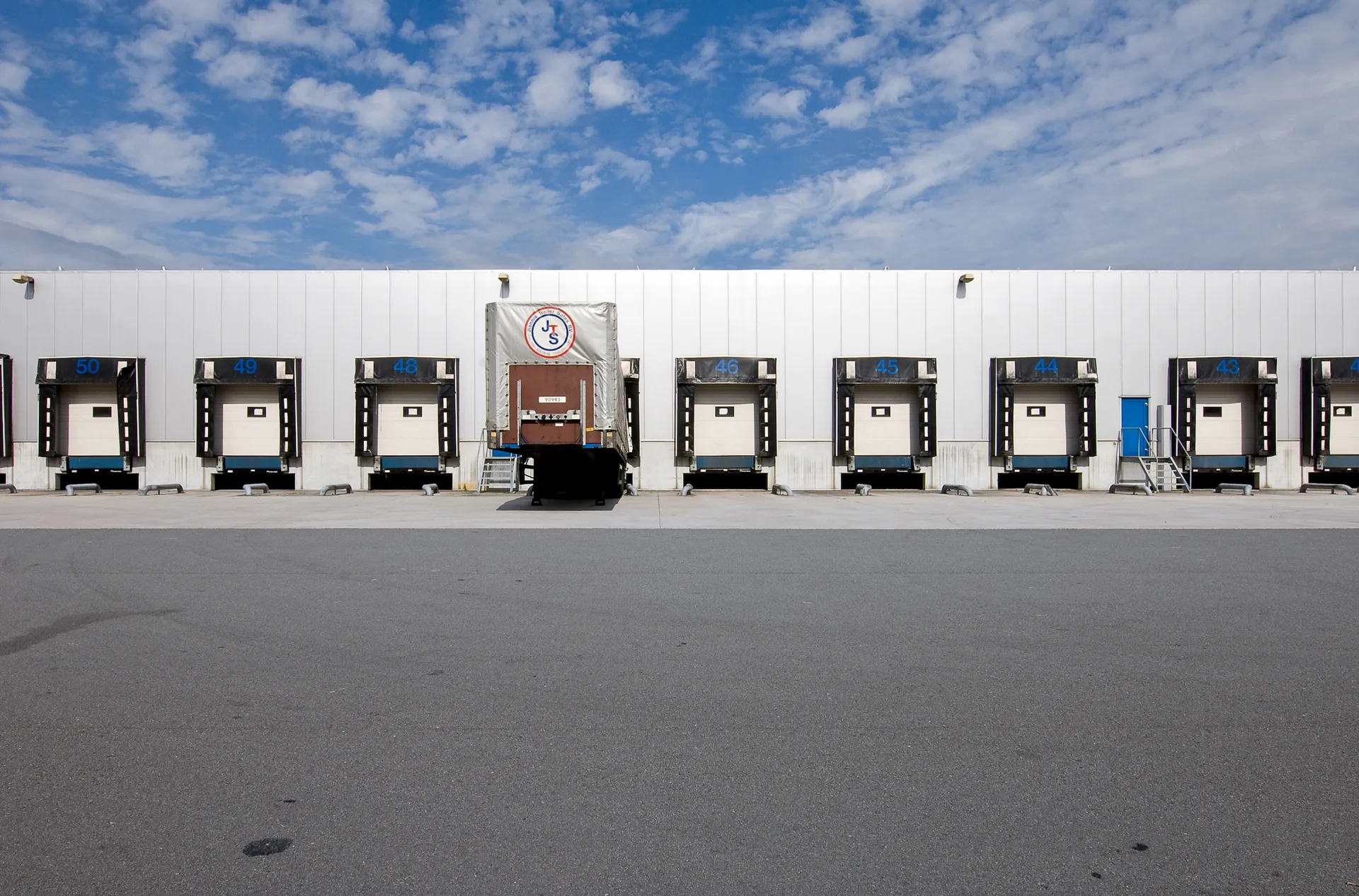Een groot industrieel magazijn met diverse loading docks, elk met een grote roldeur.
