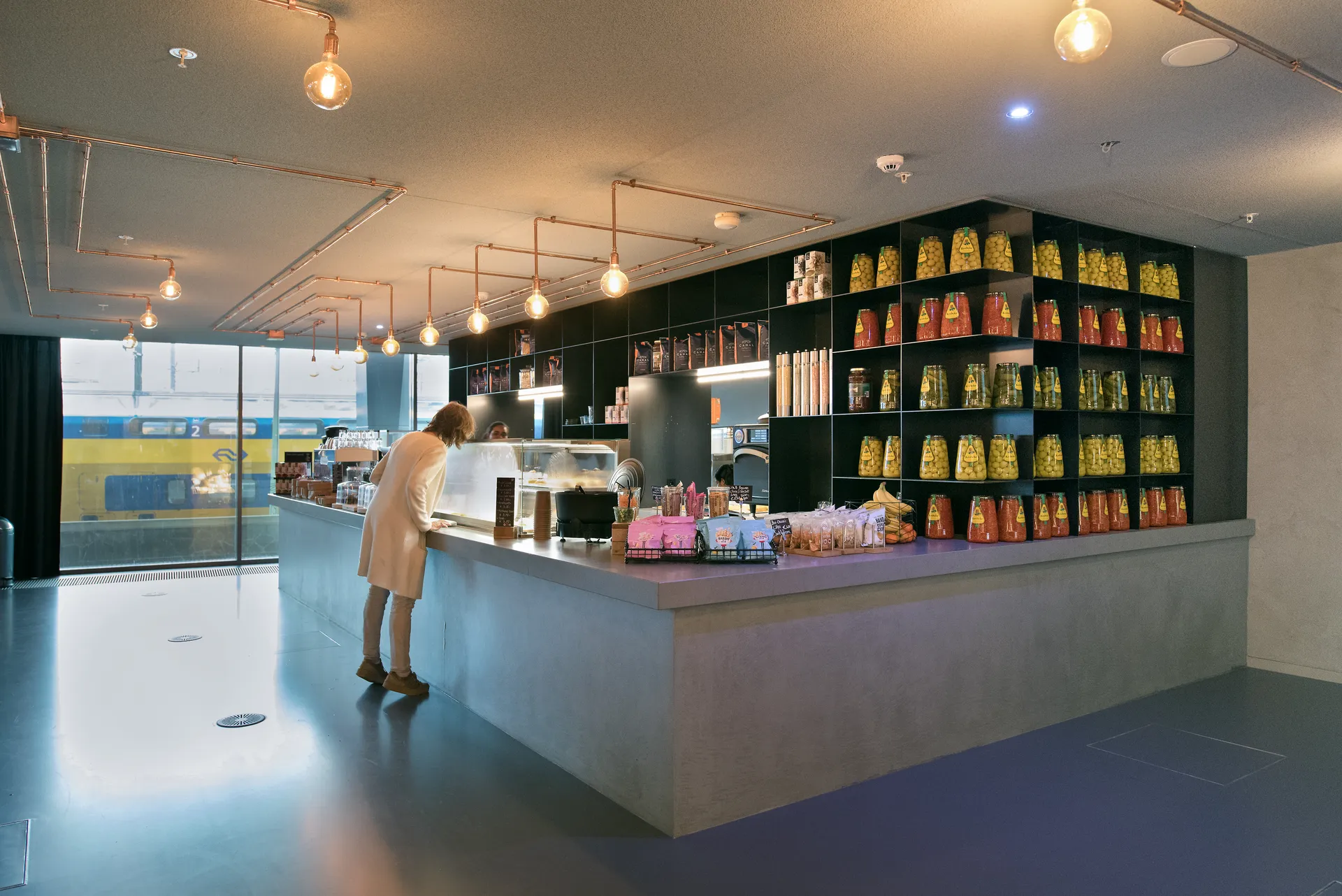 Een moderne, hippe koffieshop te zien vanaf de buitenkant met grote en hoge raampartijen en glazen deuren.