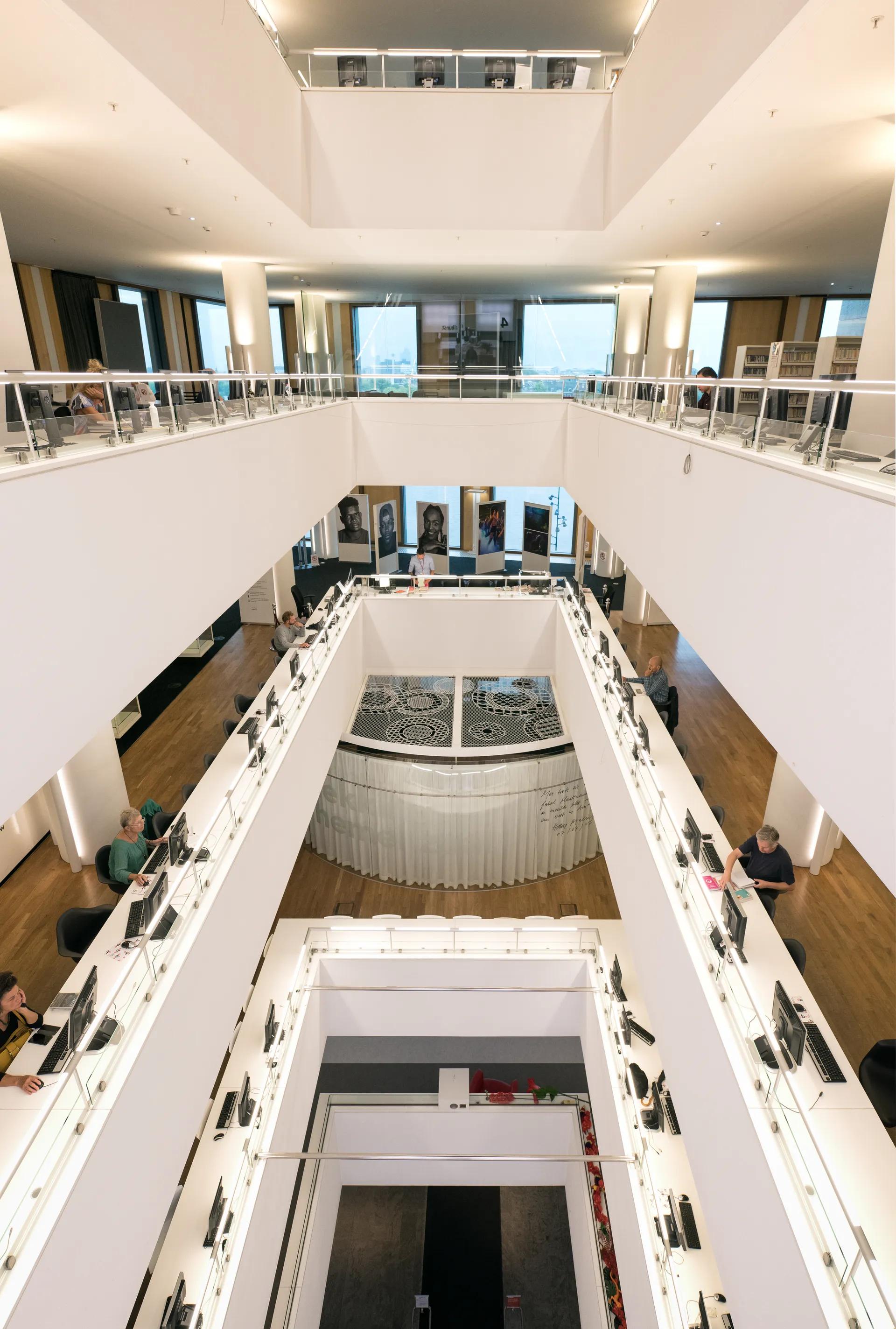 Een grote open kantoorruimte met een centraal atrium, witte muren, een hoog plafond en een overvloed aan natuurlijk daglicht.