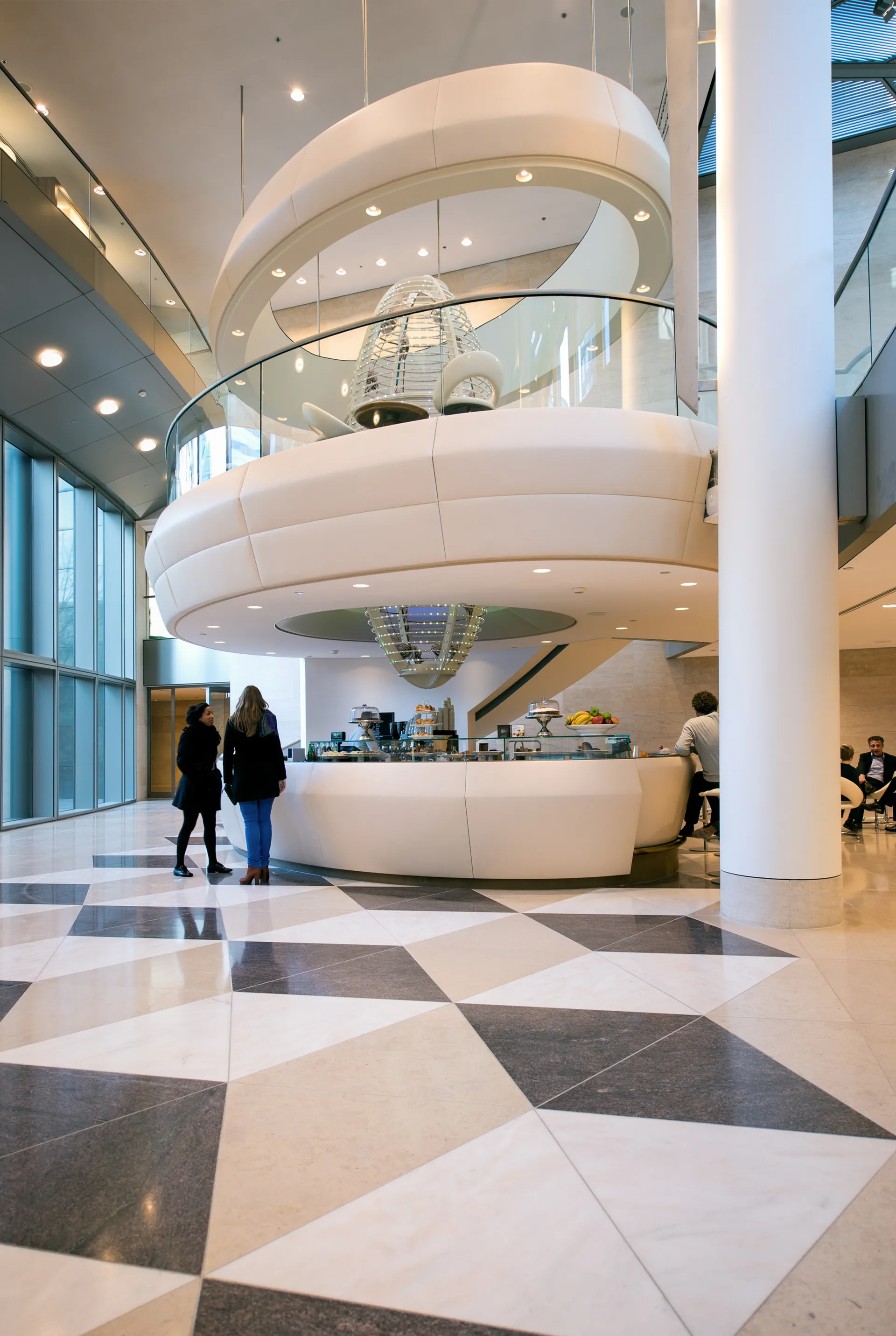 Een modern kantoor atrium met een grote witte wenteltrap, een geblokte zwart/wit-vloer en een balie met een glazen vitrine.