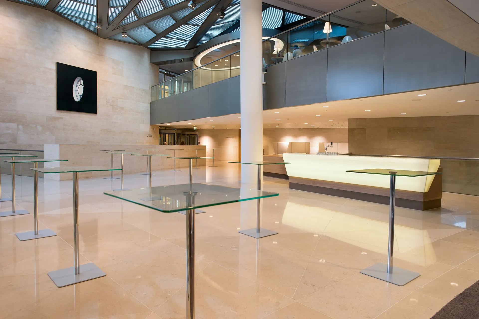 Een moderne kantoorlobby met bijzondere designtafeltjes, met veel licht dat door het glazen atrium een open sfeer geeft.